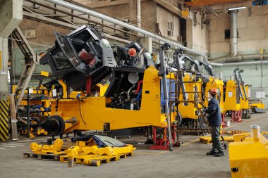 Two male workers of modern industrial plant or repairmen checking efficiency of huge construction machines in workshop