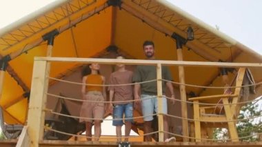 Low angle of young Biracial parents and son walking out on terrace of summer house, chatting and looking into distance on sunny day