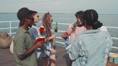 Medium long of diverse young people in sunglasses and casual clothes dancing and drinking on hot summer day