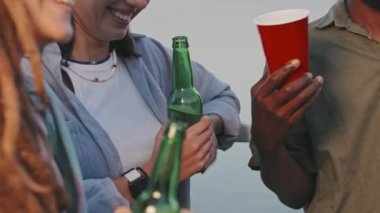Midsection of cropped guy and girls having drinks, gesticulating, laughing and talking on outdoor party in summer evening