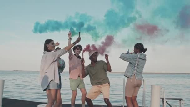 Захоплена Багатоетнічна Молодь Танцює Різнокольоровими Димовими Бомбами Пірсі Біля Озера — стокове відео