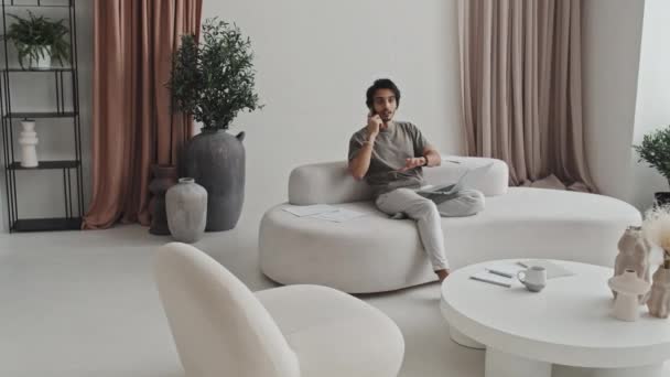 中近東の若い男性マネージャーがリビングルームに座り モダンなインテリアデザインで落ち着いた色 紙を持ち 昼間は携帯電話で話しています — ストック動画