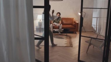 Long shot of young Asian woman and Middle Eastern man sitting on brown couch in living room in evening, having conversation about family budget