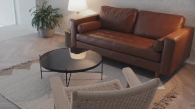 View of living room with brown leather couch, carpet, coffee table, lamp and armchair, minimalist Scandinavian interior design, no people