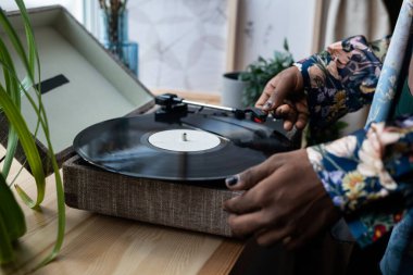 Hands of young black man with nail polish putting vinyl record on needle player standing on wooden windowsill before listening retro music clipart