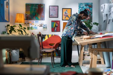 Creative guy in smart casualwear bending over wooden table while creating drawings or sketches of items for new collection