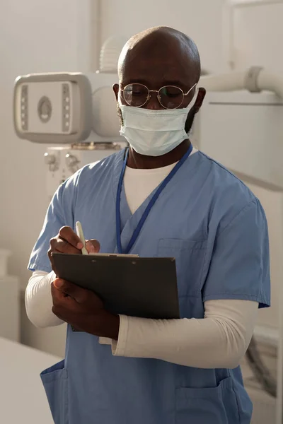 Young Serious African American Clinician Uniform Protective Mask Making Notes — Foto de Stock