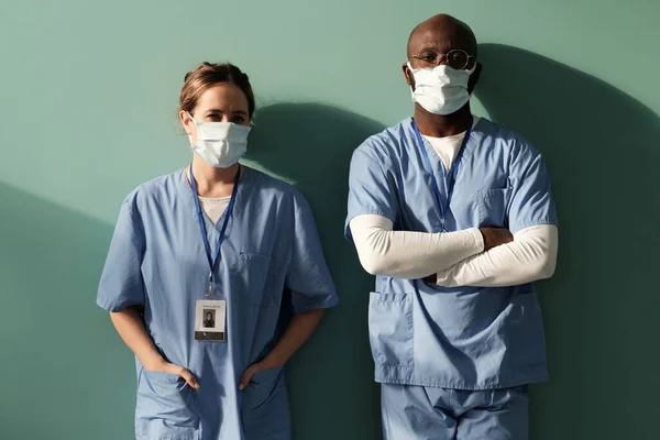 Two Young Interracial Clinicians Blue Medical Scrubs Protective Masks Standing — Foto de Stock