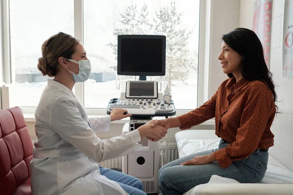 stock image Side view of female clinician and patient shaking hands in medical office while sitting in front of one another against ultrasound machine