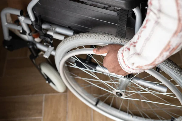 Above view of hand of young man with disability rotating wheel of wheelchair while moving down wooden floor