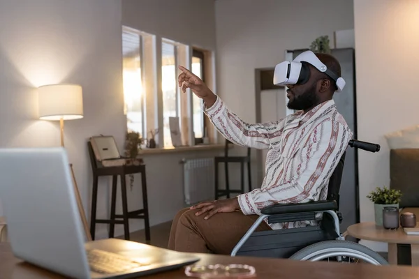 African American man with disability preparing virtual presentation while sitting in wheelchair by his workplace in living room at home
