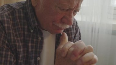 Chest-up of depressed senior Caucasian man sitting indoors at daytime, thinking