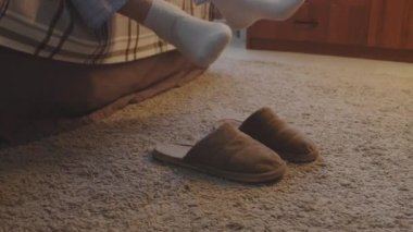 Low section of unrecognizable person putting on slippers by bed at home in morning