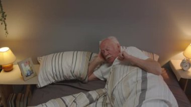 High-angle of senior Caucasian man with mustache waking up alone in his bed, looking at picture of wife in frame in morning