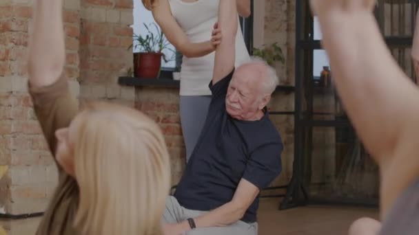 Tilting Blonde Female Yoga Instructor Helping Senior Man Who Stretching — Vídeo de Stock