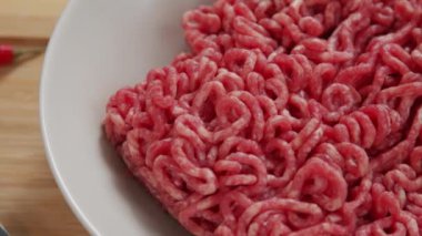 Macro tracking shot of raw ground beef meat in white ceramic bowl