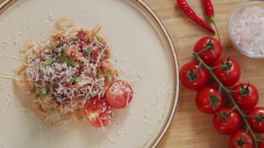 Top down close up shot of freshly cooked spaghetti bolognese served on plate on wooden kitchen table with fresh cherry tomatoes, sea salt and hot peppers