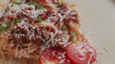 Close up tracking shot of homemade spaghetti bolognese served with fresh cherry tomatoes and grated Parmesan cheese on top