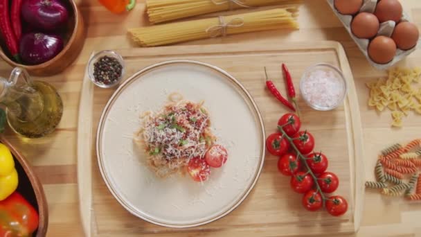 パスタ スパイスと木製のキッチンテーブルの上にすりおろしたチーズと新鮮なトマトを添えてスパゲティボロネーゼのトップダウンショット — ストック動画