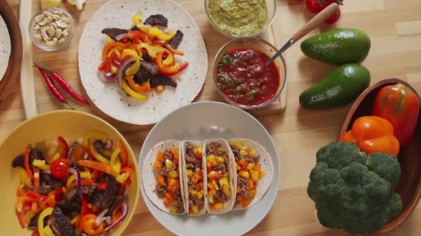 肉や野菜を詰めメキシコのタコスのトップダウンショットや木製のキッチンテーブルの上に様々な食品成分 — ストック動画