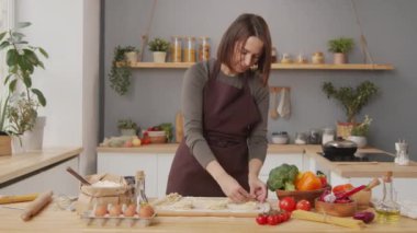 Woman in apron twirling fresh homemade pasta into nests for drying while cooking in kitchen