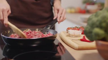 Close up tracking shot of woman stirring ground beef meat in frying pan with wooden spatula while cooking meal at home