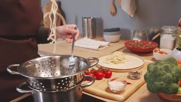 新鮮に調理された自家製パスタをザルから取り 自宅でキッチンで夕食を作りながら プレート上でそれを提供するエプロンの女性の作物のショット — ストック動画