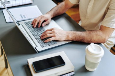 Hands of young businessman typing on laptop keyboard by his workplace while analyzing online financial data