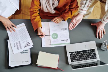 Above view of group of economists discussing financial documents with data at meeting while businessman explaining statistics