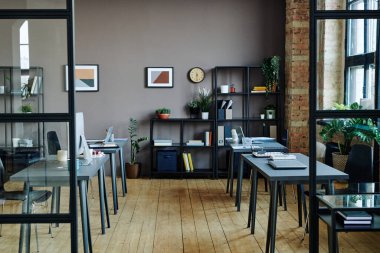Interior of spacious modern openspace office with computers on desks, shelves with documents and green plants and pictures on wall