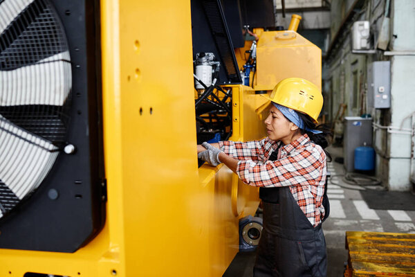 Young female engineer with damaged hand or arm standing by industrial machine during process of repairment in workshop