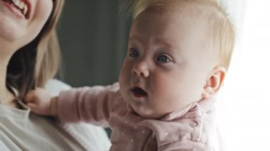 Medium close-up of cute blue-eyed Biracial infant in hands of cropped parent at daytime at home