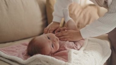 Locked down of cute blue-eyed Biracial baby girl lying on back on couch, cropped parent standing and lifting her up by hands