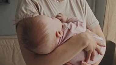 Tilting up of young Biracial woman rocking baby to sleep at home in afternoon, infant in pink onesie with pacifier