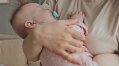 Midsection of cropped woman rocking cute sleepy baby at home in afternoon, infant in pink onesie with pacifier