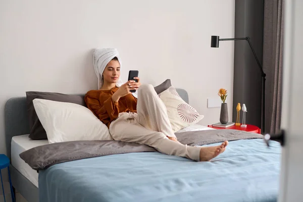 Young Restful Female Home Wear Sitting Double Bed Texting Mobile — ストック写真