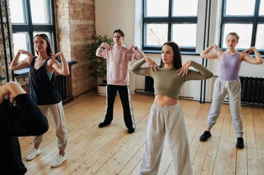 Large group of teenagers exercising in spacious loft studio with their hands on shoulders while standing in front of instructor or leader