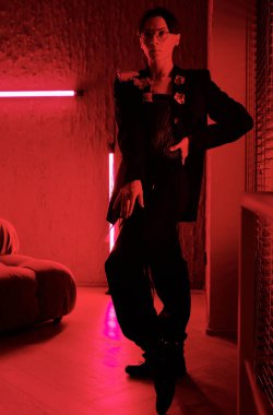 Posh young man in smart black attire performing vogue dance movements in red lit room of contemporary entertainment club