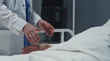Midsection slow motion of cropped doctor holding hand of unrecognizable patient lying in hospital bed in ward