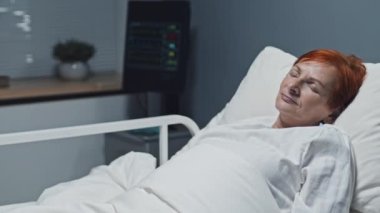 Medium of mature red-haired Caucasian woman sleeping in hospital bed and smiling