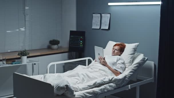 침대에 누워있는 성숙한 짧은머리 코카서스 여성의 태블릿 컴퓨터를 사용하여 — 비디오