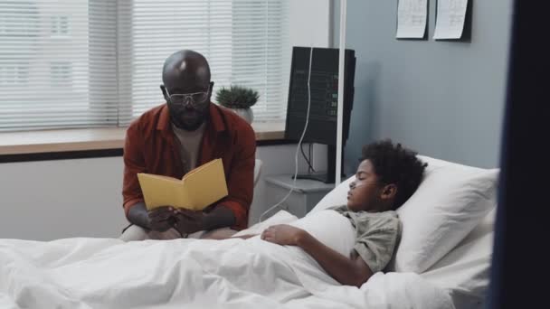 Средний Возраст Молодого Чернокожего Человека Читающего Книгу Бессознательному Маленькому Сыну — стоковое видео