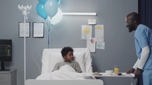 Запертый Симпатичный Афроамериканец Лежит Больничной Койке Молодой Медбрат Приносит Завтрак — стоковое видео