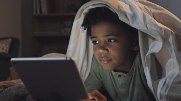 Грудь Симпатичного Черного Мальчика Лежит Животе Одеялом Постели Используя Планшетный — стоковое видео