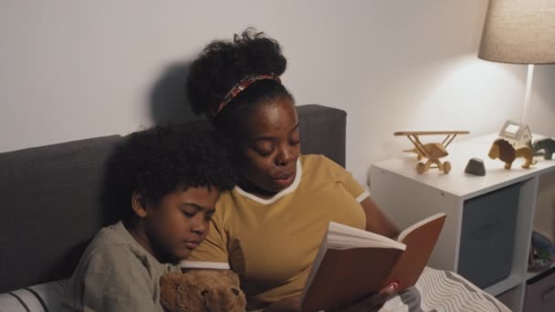 中等年龄的非洲裔美国母亲给9岁可爱的儿子读书 晚上躺在床上 抱着玩具熊睡觉 — 图库视频影像