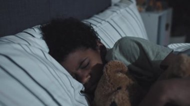 Medium of cute Black boy hugging stuffed bear, sleeping in his bed at home at night, having nightmare, waking up