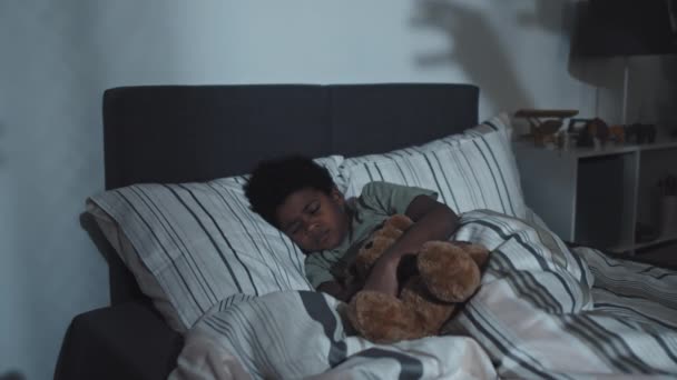 Средний Девятилетний Чернокожий Мальчик Обнимает Игрушечного Медведя Спит Дома Темноте — стоковое видео