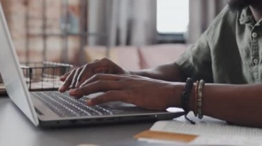 Low angle of hands of unrecognizable man sitting at desk indoors at daytime, typing on keyboard of laptop computer