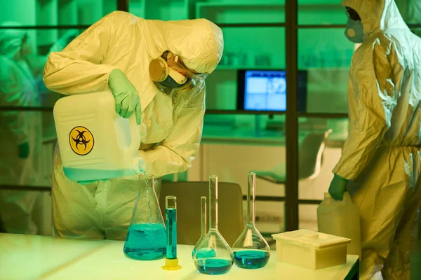 One Three Scientists Protective Coveralls Respirators Pouring Blue Liquid Big — Stock Photo, Image