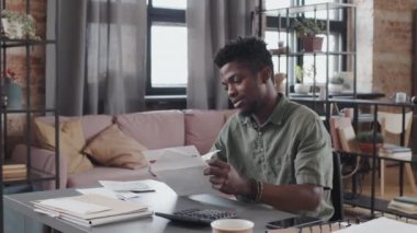 Waist-up of young joyous African American man sitting at desk in living room at daytime, opening envelope with letter, looking happy